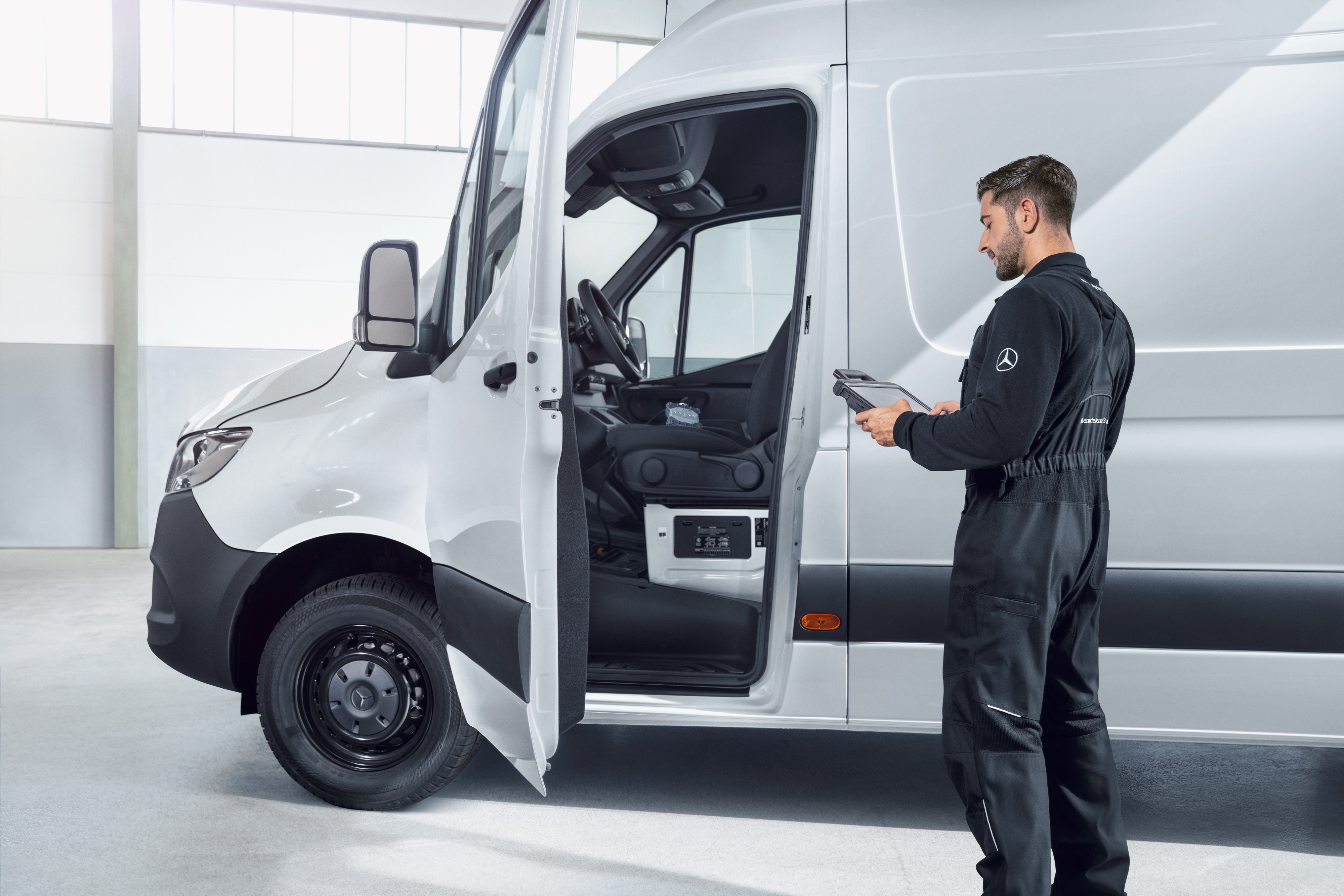 Mercedes-Benz | Přehled kvality dodávkových vozidel Mechanik kontroluje bílé dodávkové vozidlo Mercedes-Benz pomocí tabletu, což symbolizuje standardy kvality a příslib kvality.