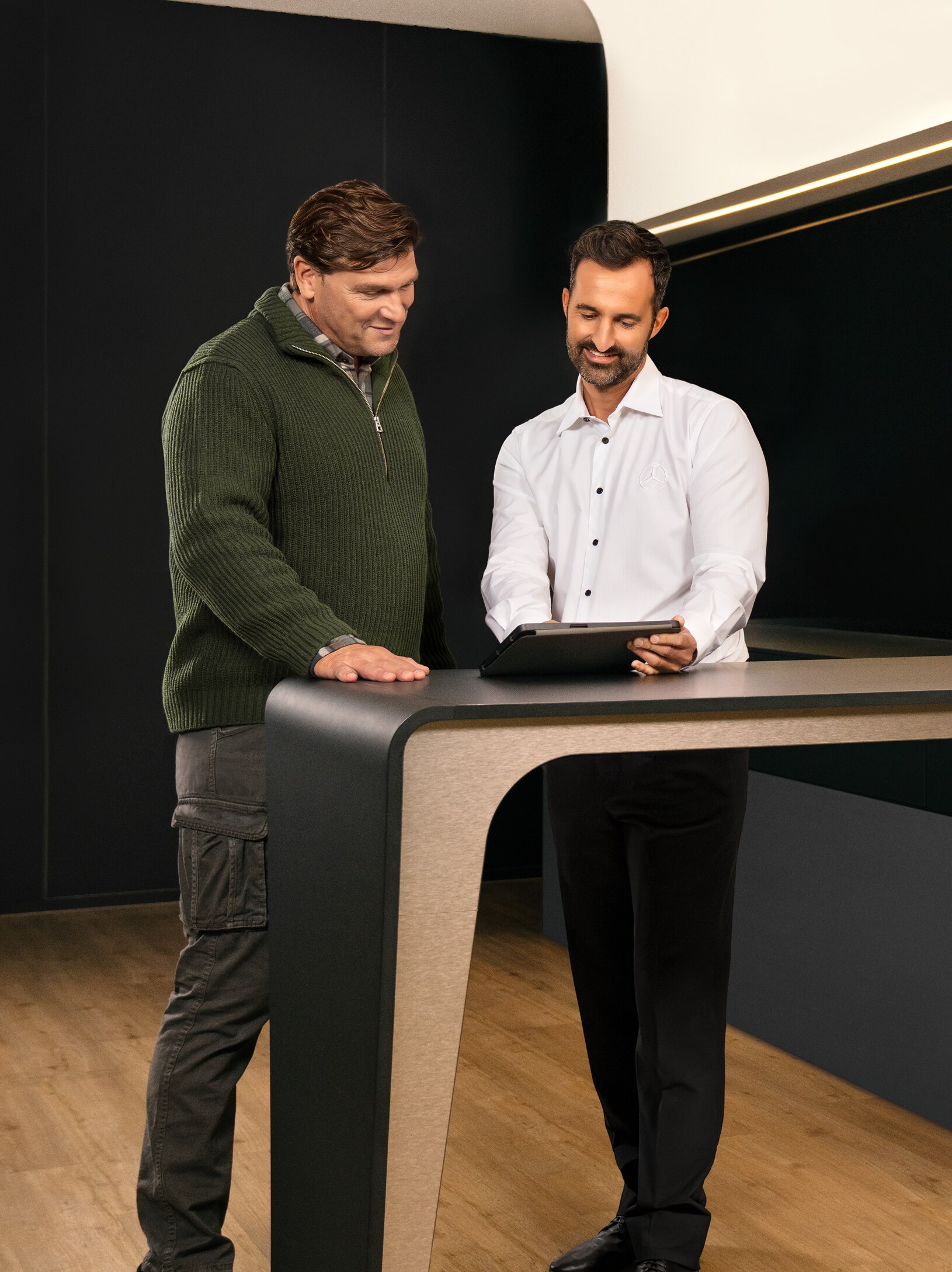 Dva muži stojí kolem stolu, konzultují a&nbsp;přitom se dívají na iPad.