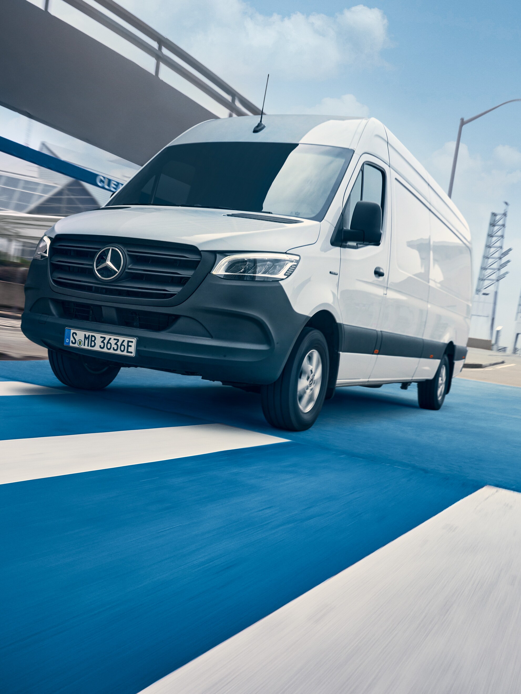 Bílý vůz Mercedes-Benz Sprinter jede po silnici městem.