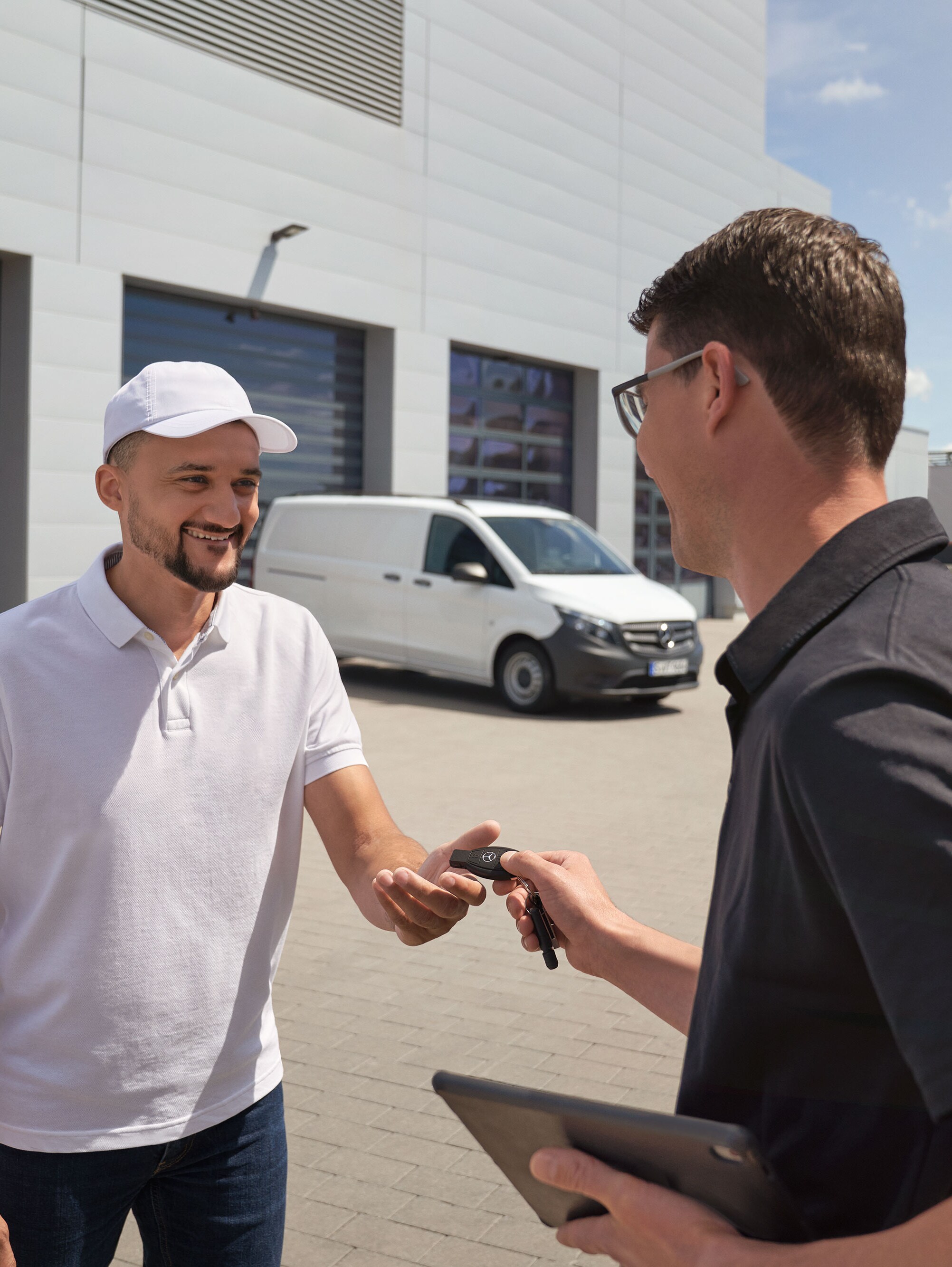 Technik předává klíček zákazníkovi, v&nbsp;pozadí je bílé dodávkové vozidlo Mercedes-Benz Vito.