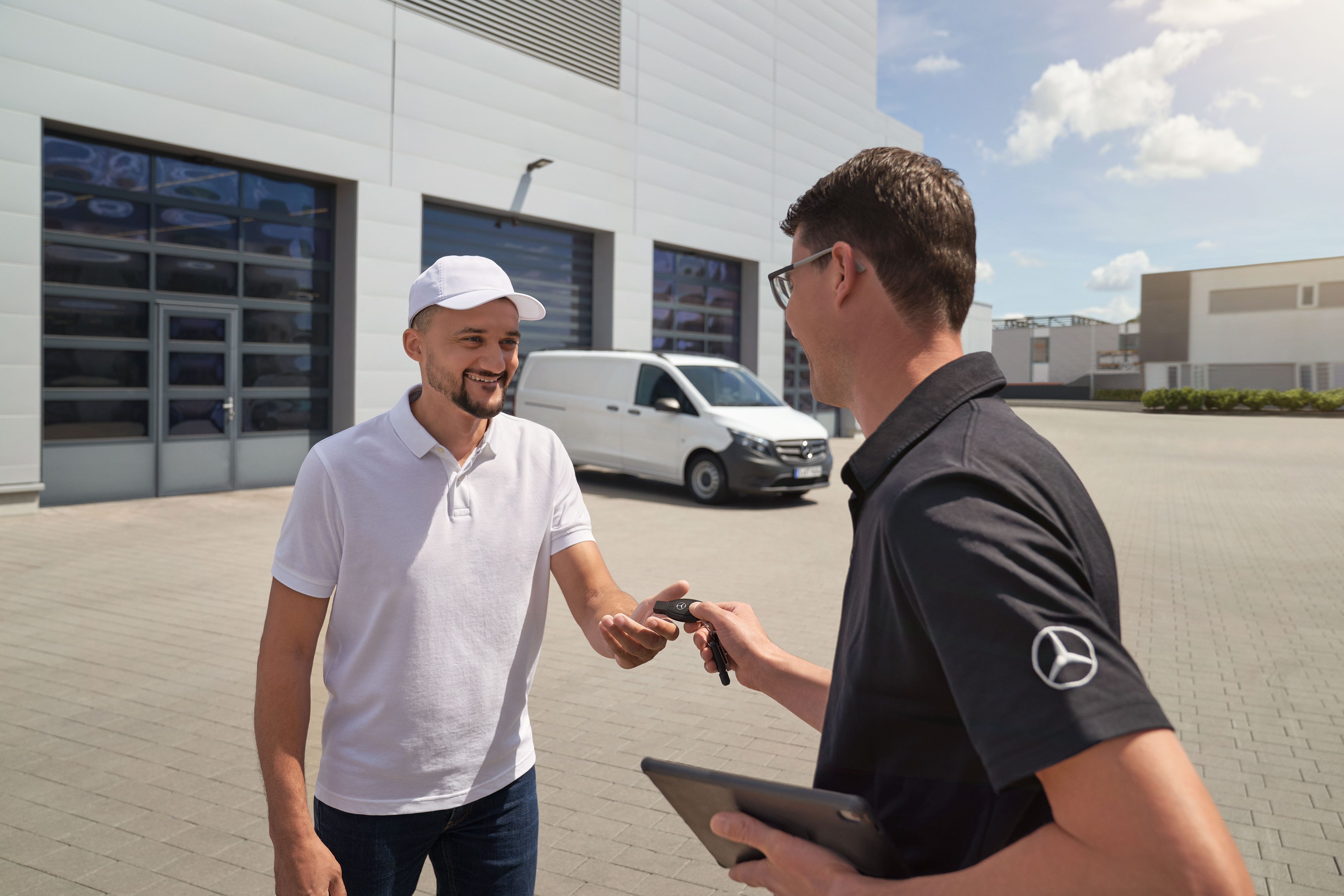 Mercedes-Benz | ServiceCare pro dodávkové vozidlo | Doplňkové služby Technik předává klíček zákazníkovi, v pozadí je bílé dodávkové vozidlo Mercedes-Benz Vito.