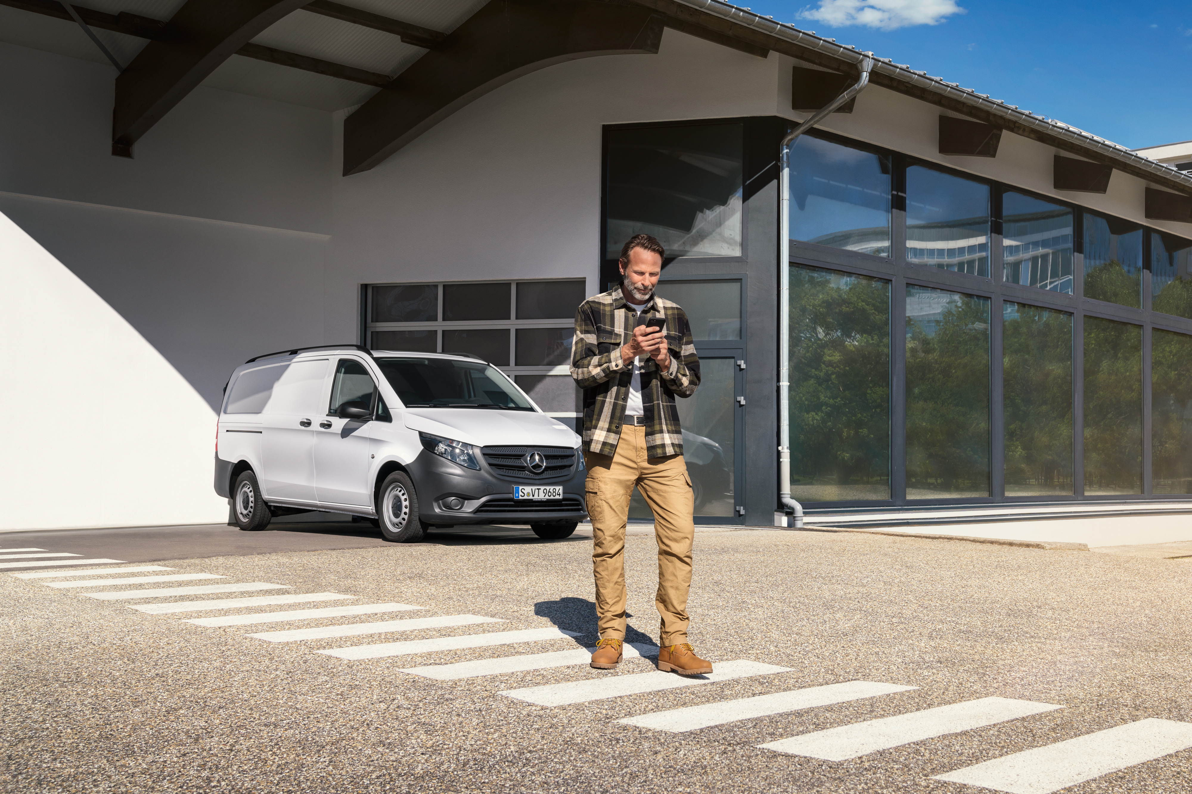 Mercedes-Benz | Servis pro elektromobily | Digitální podpora Muž stojící před bílým dodávkovým vozidlem Mercedes-Benz Vito a používající svůj chytrý telefon.