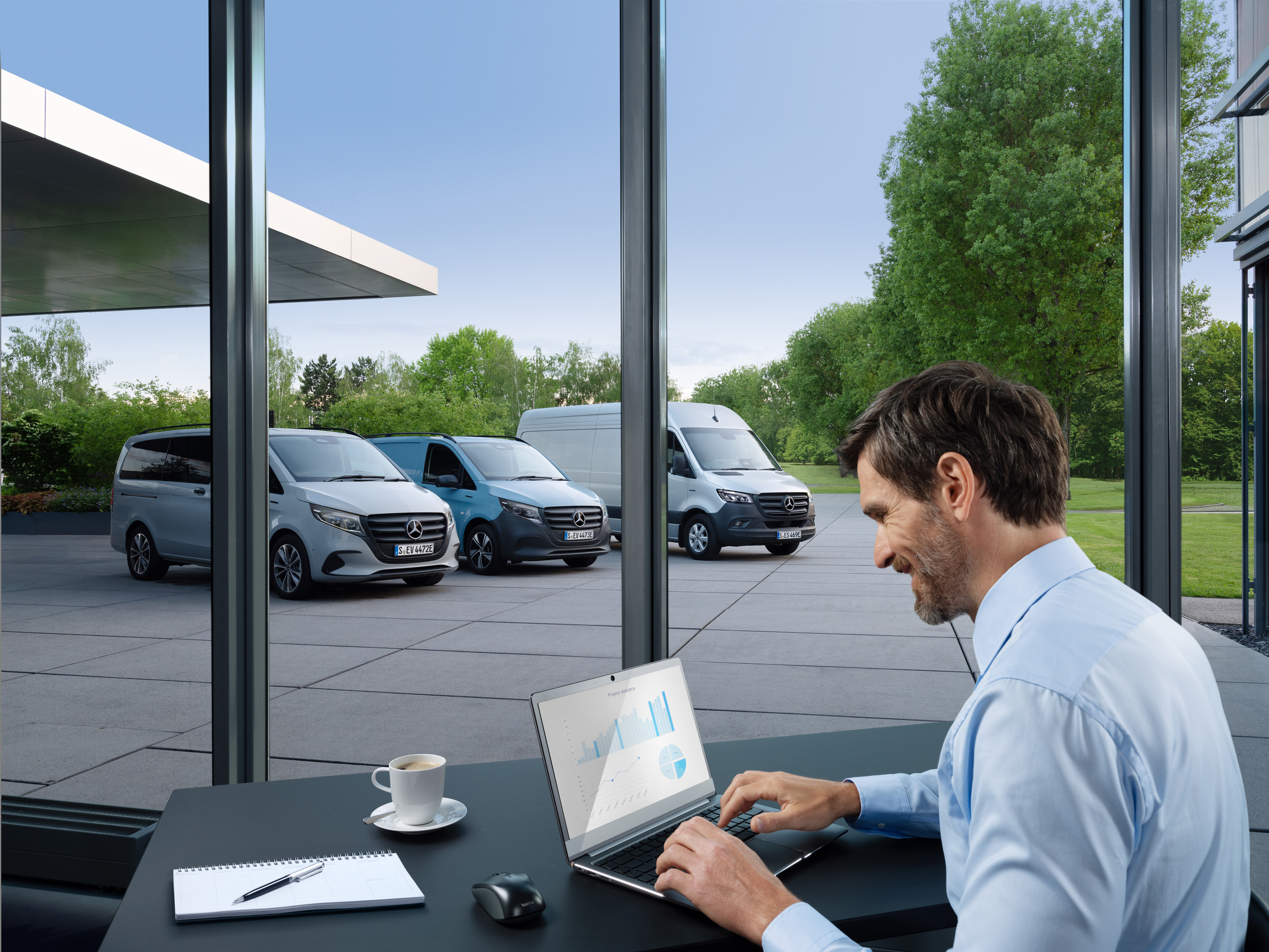 Mercedes-Benz | Servis pro elektromobily | Smlouvy Muž pracuje na notebooku, venku je řada dodávkových vozidel Mercedes-Benz.