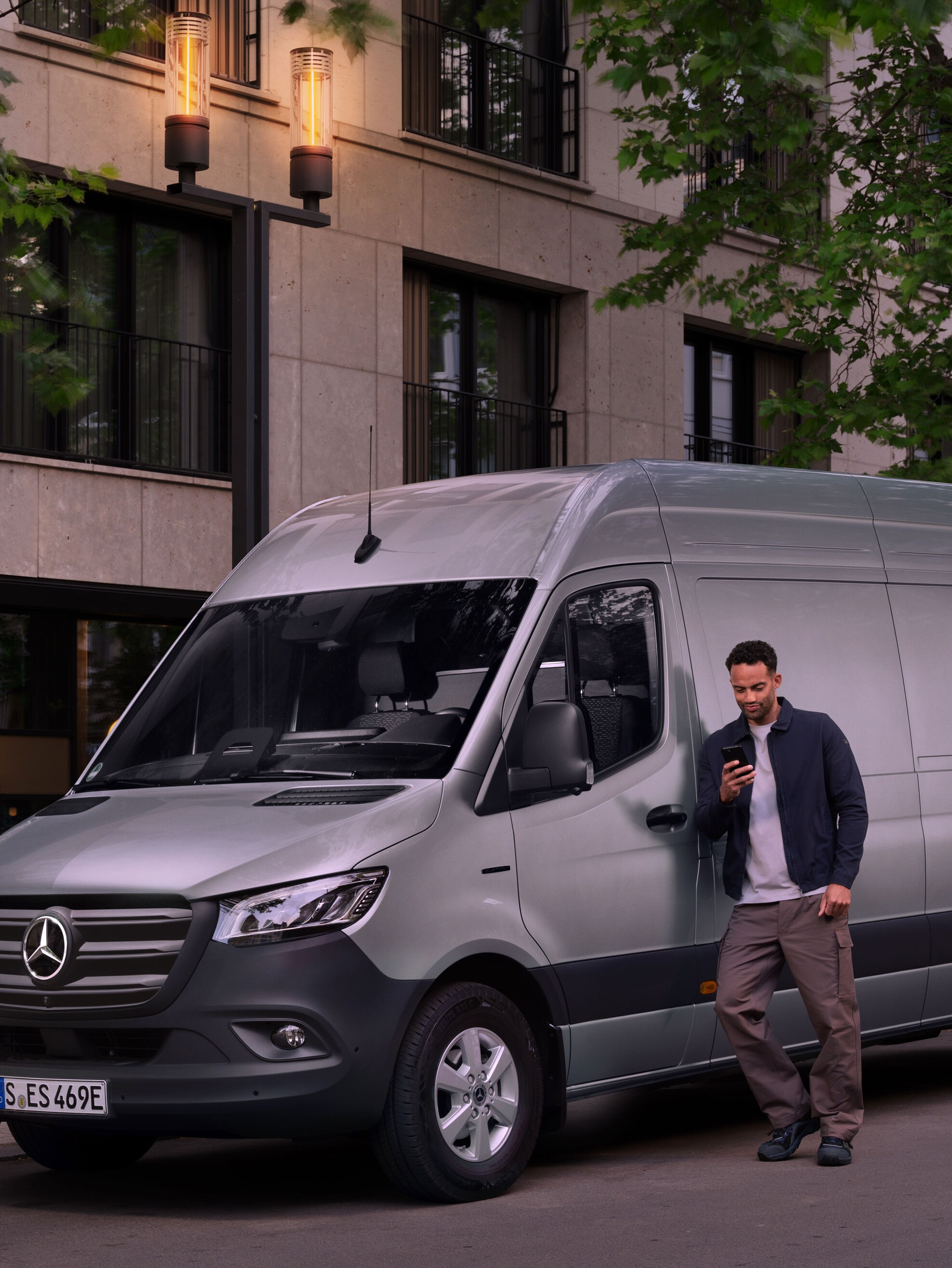 Muž se opírá o&nbsp;stříbrný Mercedes-Benz Sprinter a&nbsp;vyplňuje zprávu o&nbsp;škodách na svém mobilním telefonu.