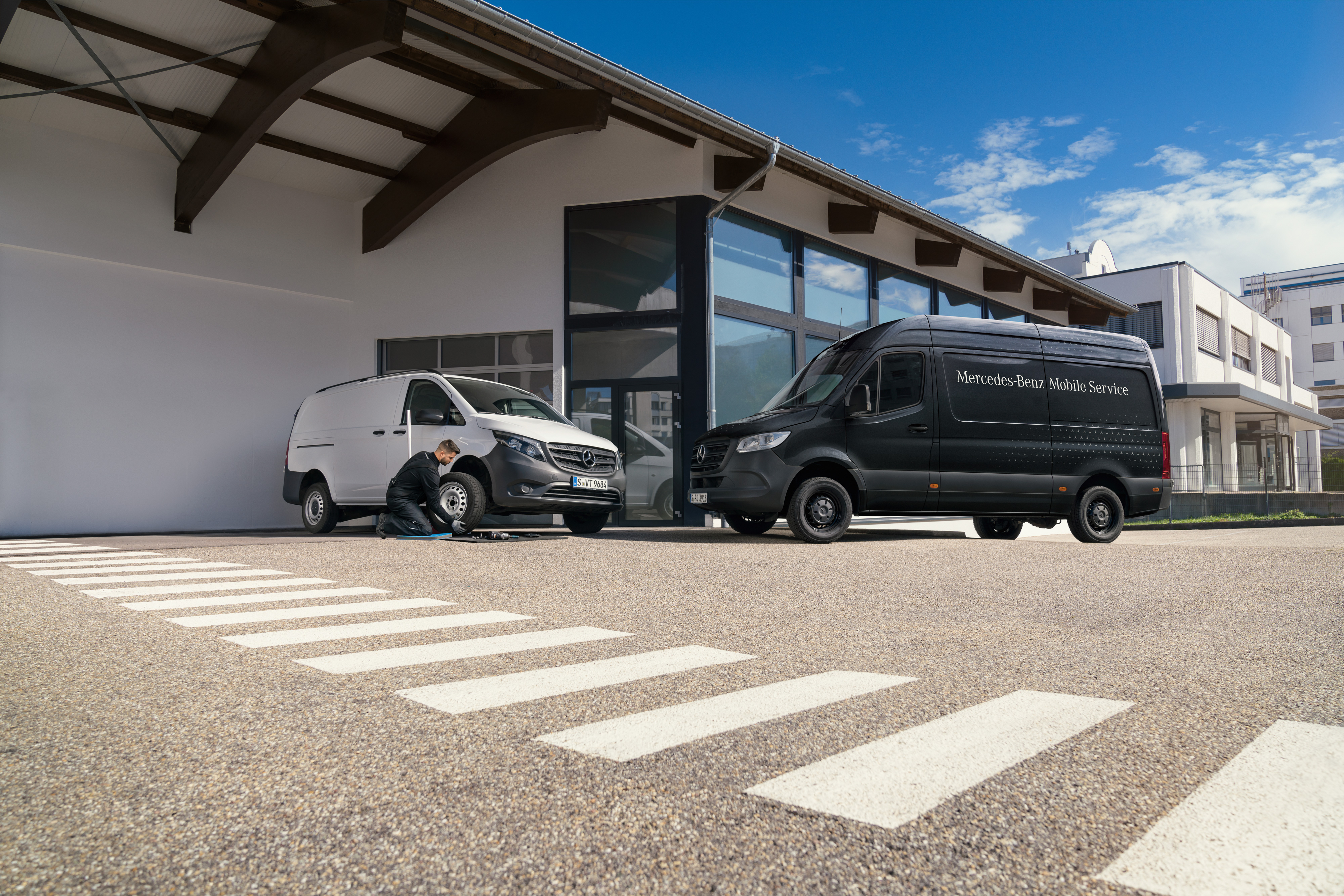 Mercedes-Benz | Mobilní servis | Brzdová soustava Technik mění pneumatiku na bílém dodávkovém vozidle Mercedes-Benz Vito před showroomem.