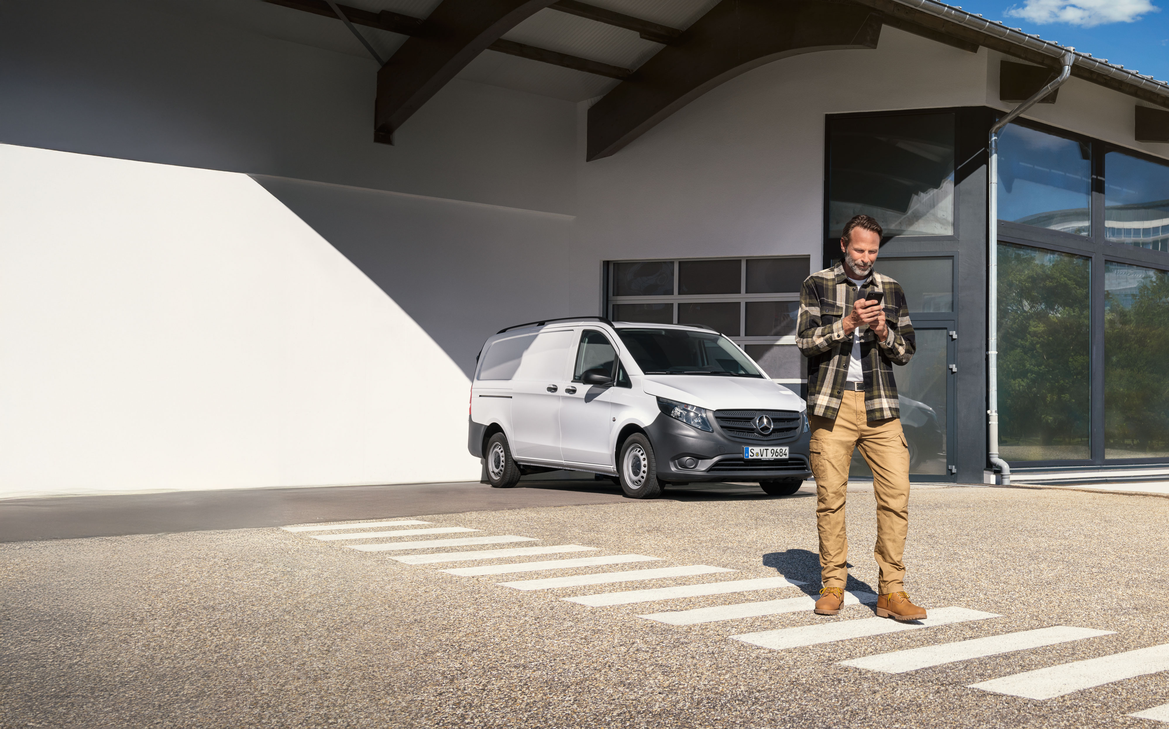 Mercedes-Benz | Maintenance | Appointment booking Customer books an appointment using his mobile device while standing infront of a white Mercedes-Benz Vito van.
