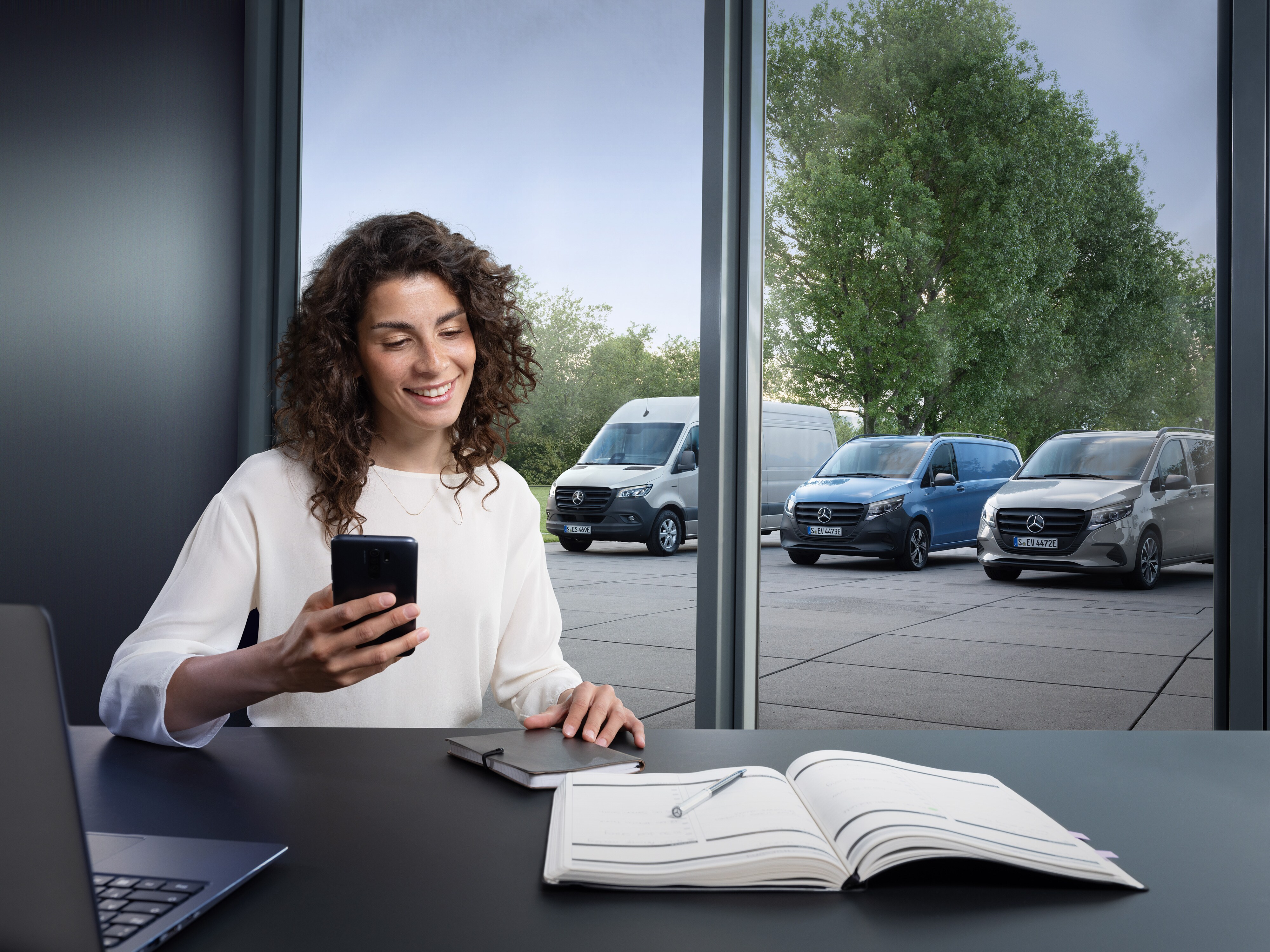 Žena dělá plány na svém chytrém telefonu před svým dodávkovým vozidlem Mercedes-Benz