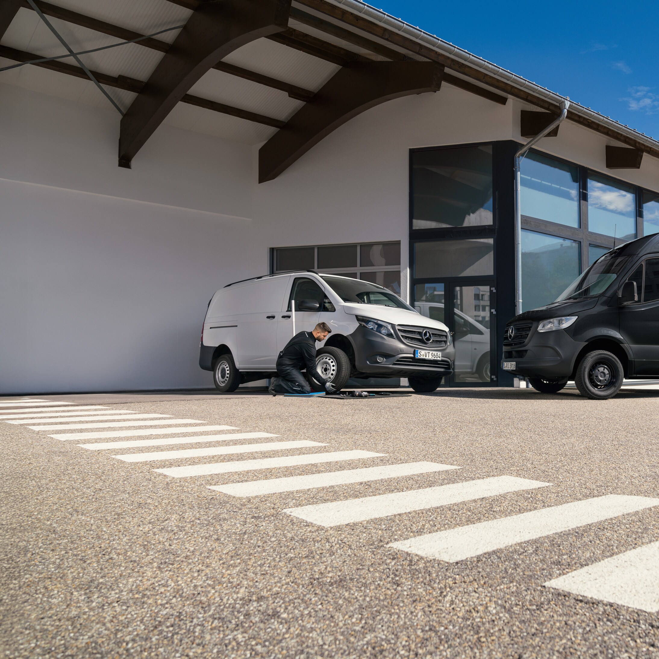 A technician replaces a trye on a white Mercedes-Benz Vito vans in a carpark.