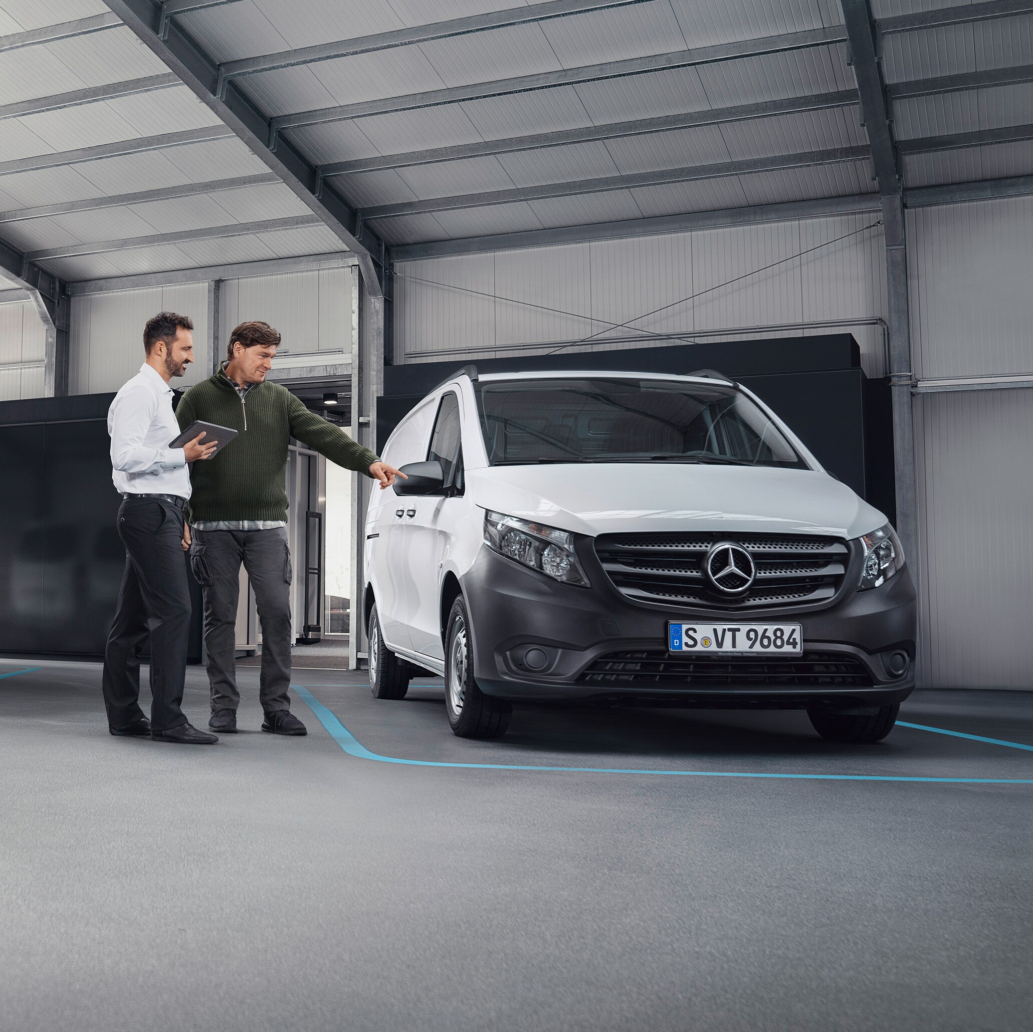 Agent zákaznické podpory Mercedes-Benz se zákazníkem v&nbsp;partnerské servisní pobočce před dodávkovými vozidlem.