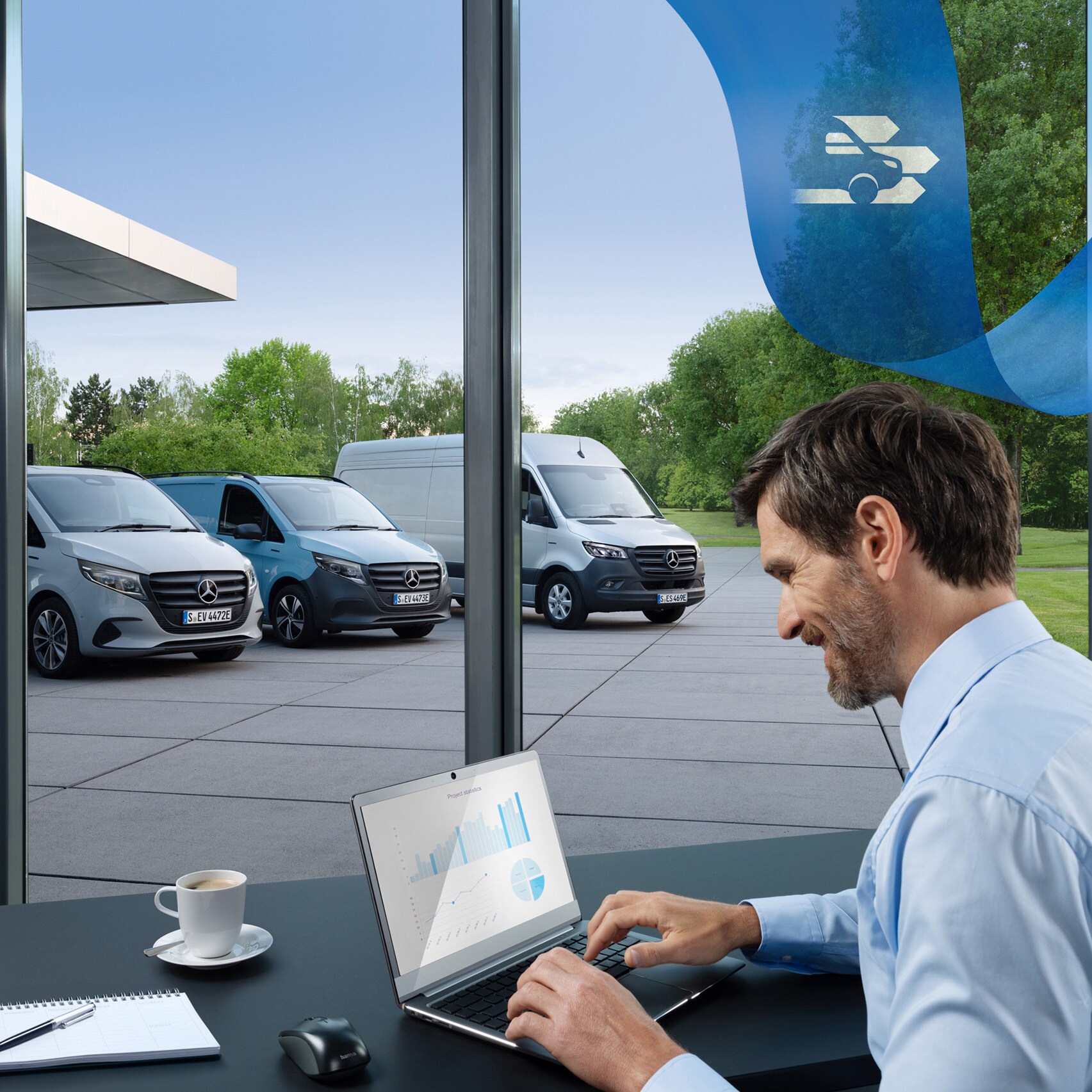 Muž používá notebook v&nbsp;kanceláři s&nbsp;řadou dodávkových vozidel Mercedes-Benz v&nbsp;pozadí.