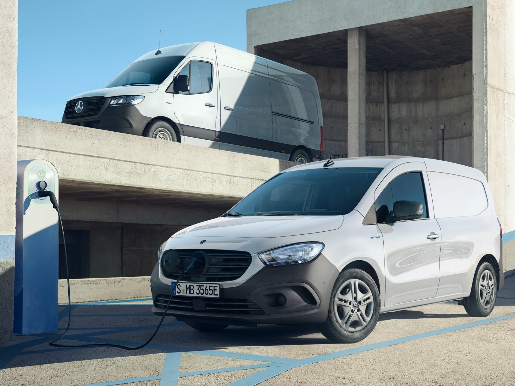eSprinter, elektrické dodávkové vozidlo od Mercedes-Benz, je připojeno k nabíjecí stanici k nabíjení. V pozadí jsou další elektrická dodávková vozidla.